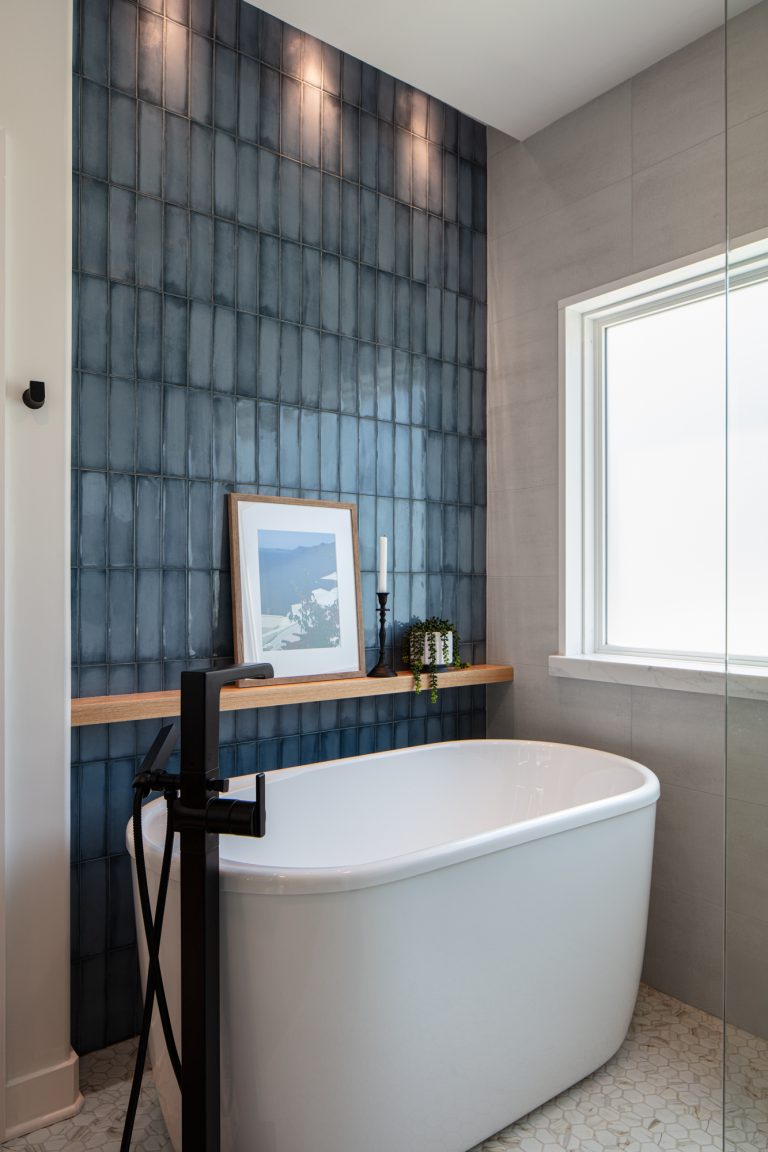Custom stand-alone white bathtub in blue-tiled bathroom